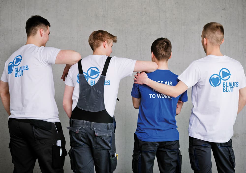 BOGE Azubis stehen zu viert mit dem Rücken zur Kamera nebeneinander und stützen sich gegenseitig, alle tragen BOGE Shirts