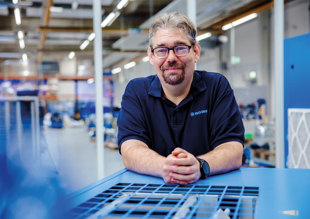 Seminarkoordinator Daniel Haufe auf blauen Kompressor gestuetzt in der BOGE Werkshalle