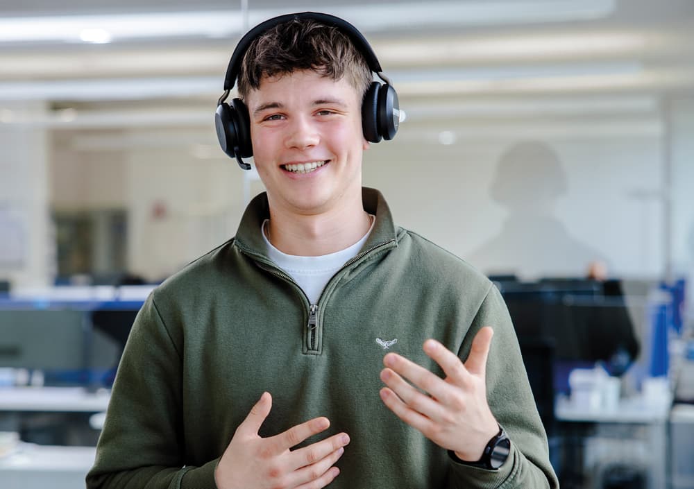 BOGE Suppor Mitarbeiter mit grünem Pulli und Headset, lächelt während eines Telefongesprächs in die Kamera