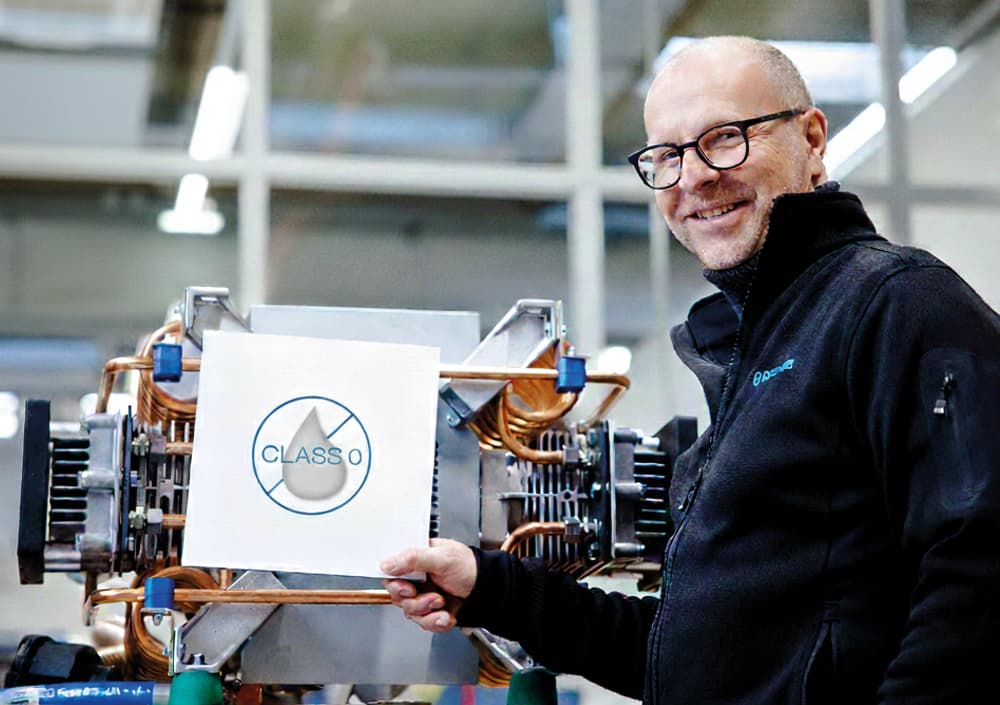 BOGE Monteur hält ein Schild mit einem Öl-Symbol welches durchgestrichen ist vor einem Ölfreien Kolbenkompressor.