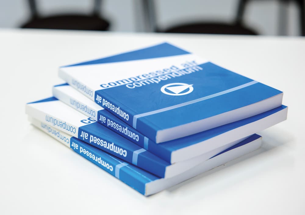 Mehrere Exemplare des BOGE Druckluft-Kompendiums in Buchform, blau-weiß, auf einem Stapel