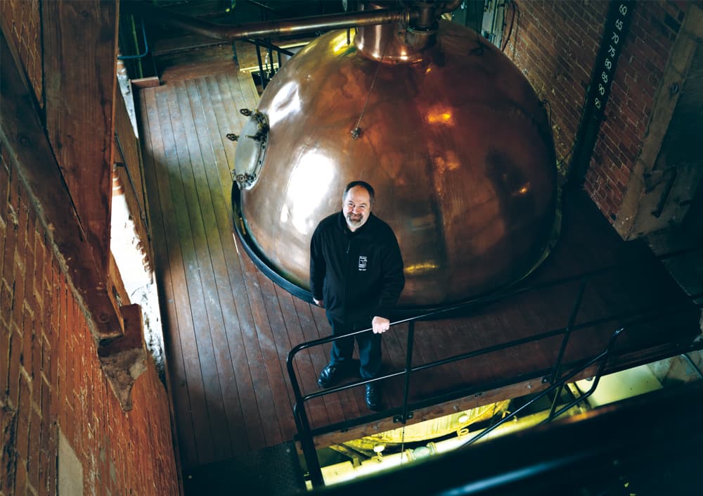 Mitarbeiter der BlackSheep Brauerei vor einem kupferfarbenen Bierkessel in einem Backsteingebäude