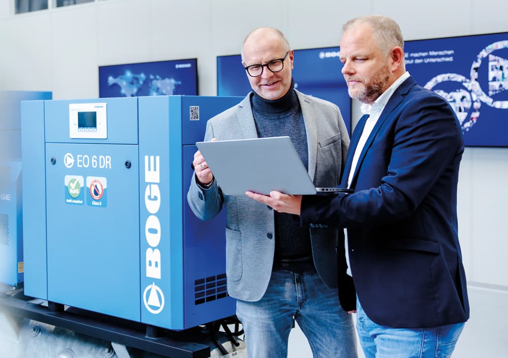 BOGE Berater mit Laptop in der Hand im Gespräch mit Kunden über einen danebenstehenden Scrollkompressor der EO-Baureihe