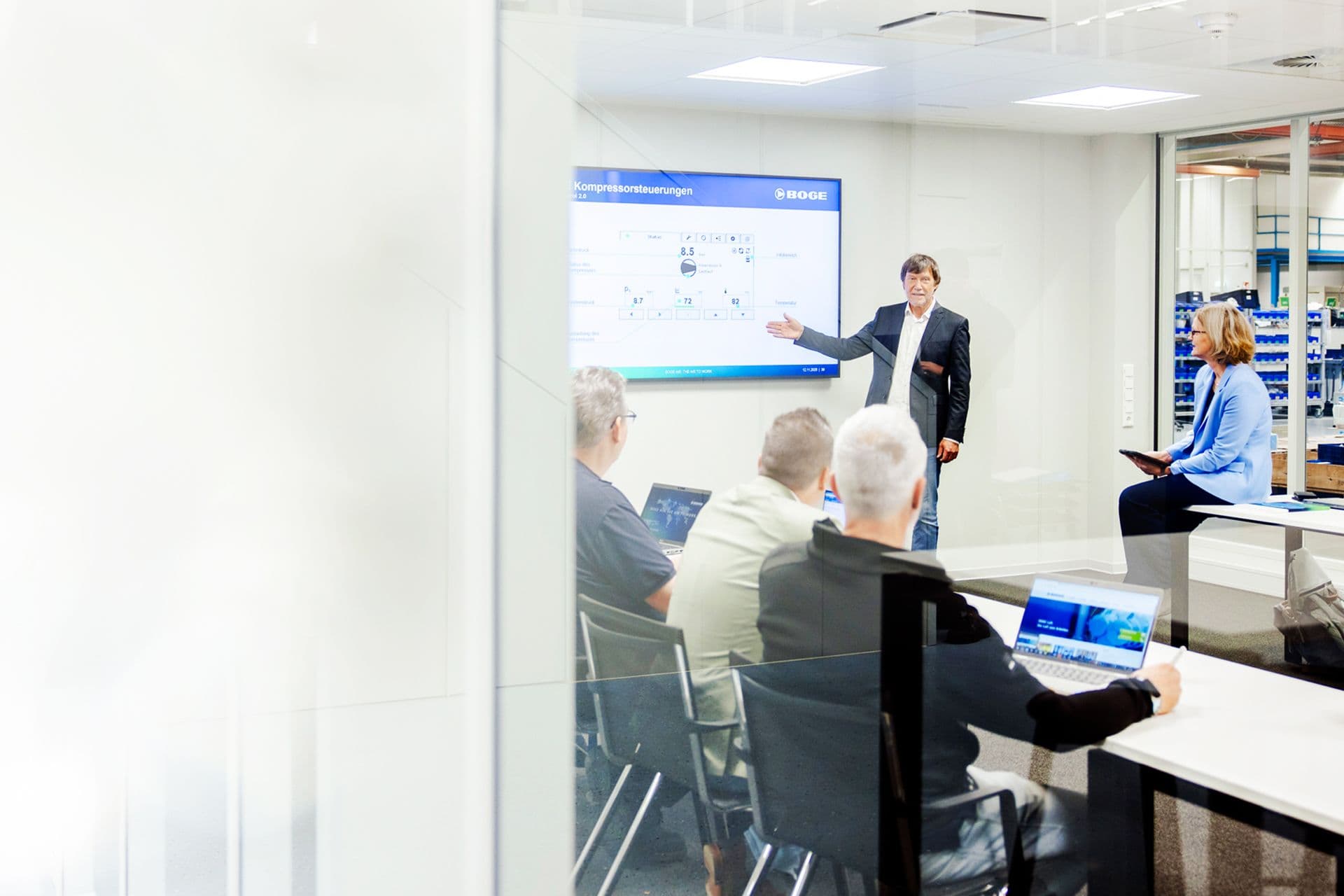 BOGE Mitarbeiter, welcher vor seinen Kollegen etwas auf einem Bildschirm erklaert.