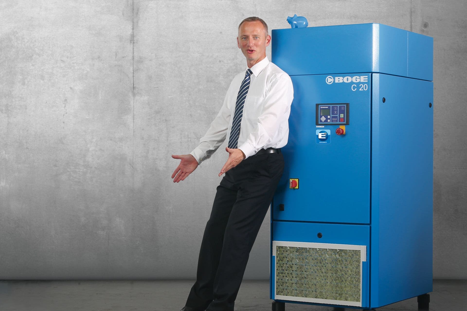 BOGE Mitarbeiter lehnt gegen den ersten Schraubenkompressor der C-Baureihe aus dem Jahr 2003. er trägt ein weißes Hemd und eine Krawatte