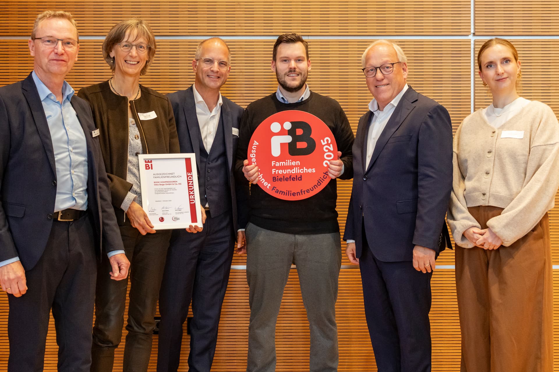 Eine Gruppe von Menschen die laechelnd in die Kamera gucken und die Auszeichnung für Familienfreundlichkeit halten