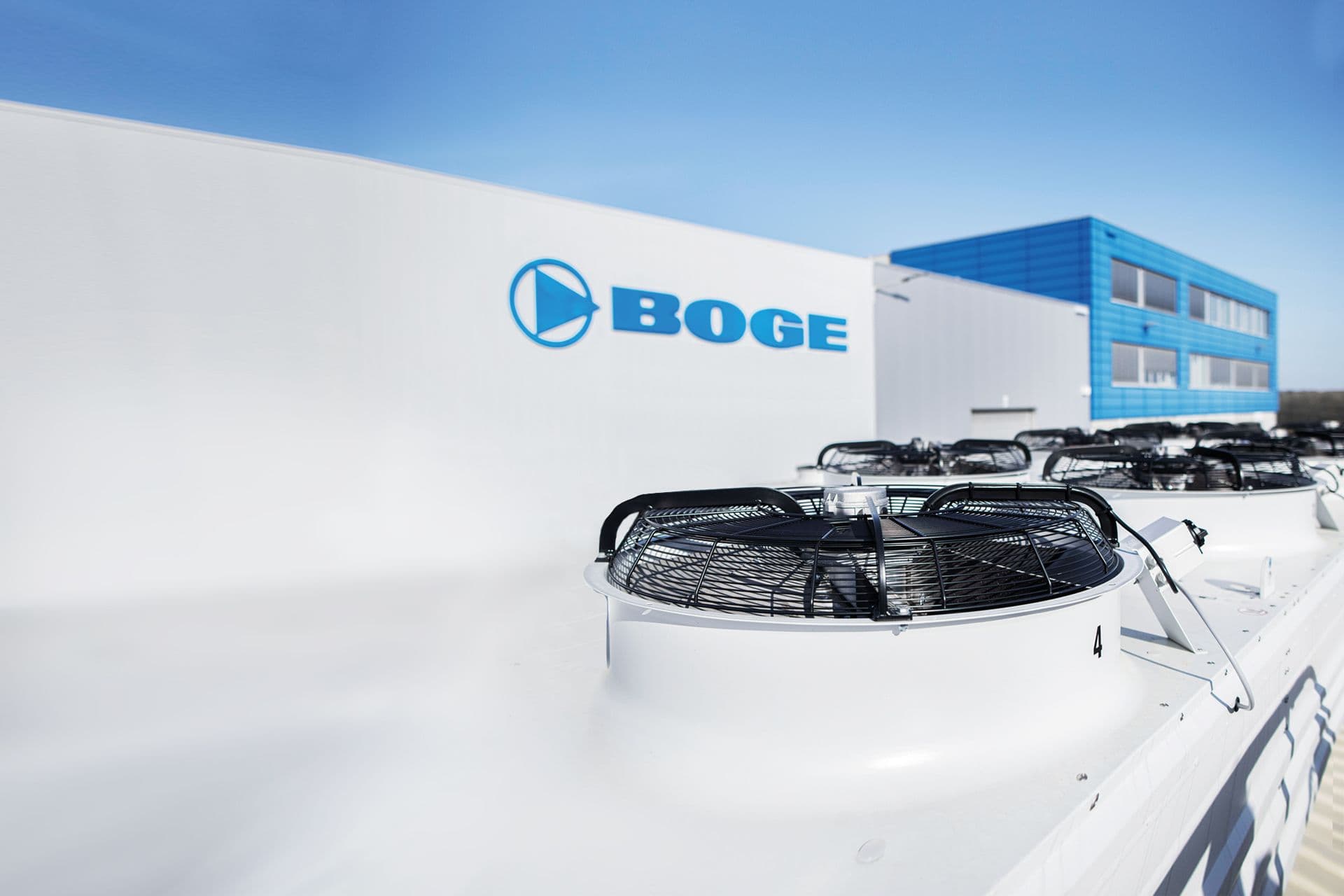 Sicht über einen weißen Container auf die weiß-blaue Gebaeudeansicht vom BOGE Hauptsitz in Bielefeld mit blauem Himmel