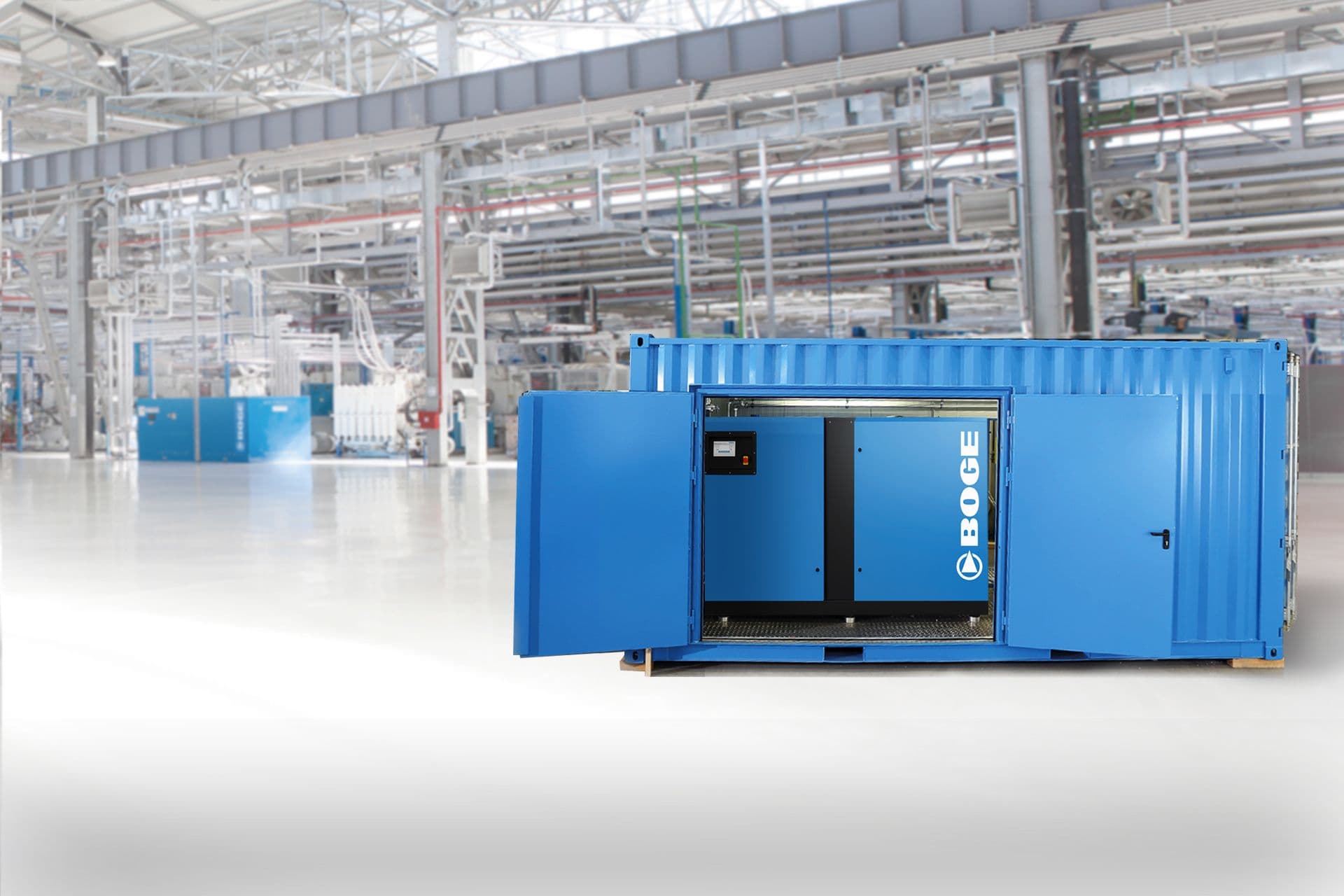 Blauer BOGE Druckluftcontainer in einer Fabrikhalle mit Kompressor, der durch geöffnete Türen zu sehen ist.