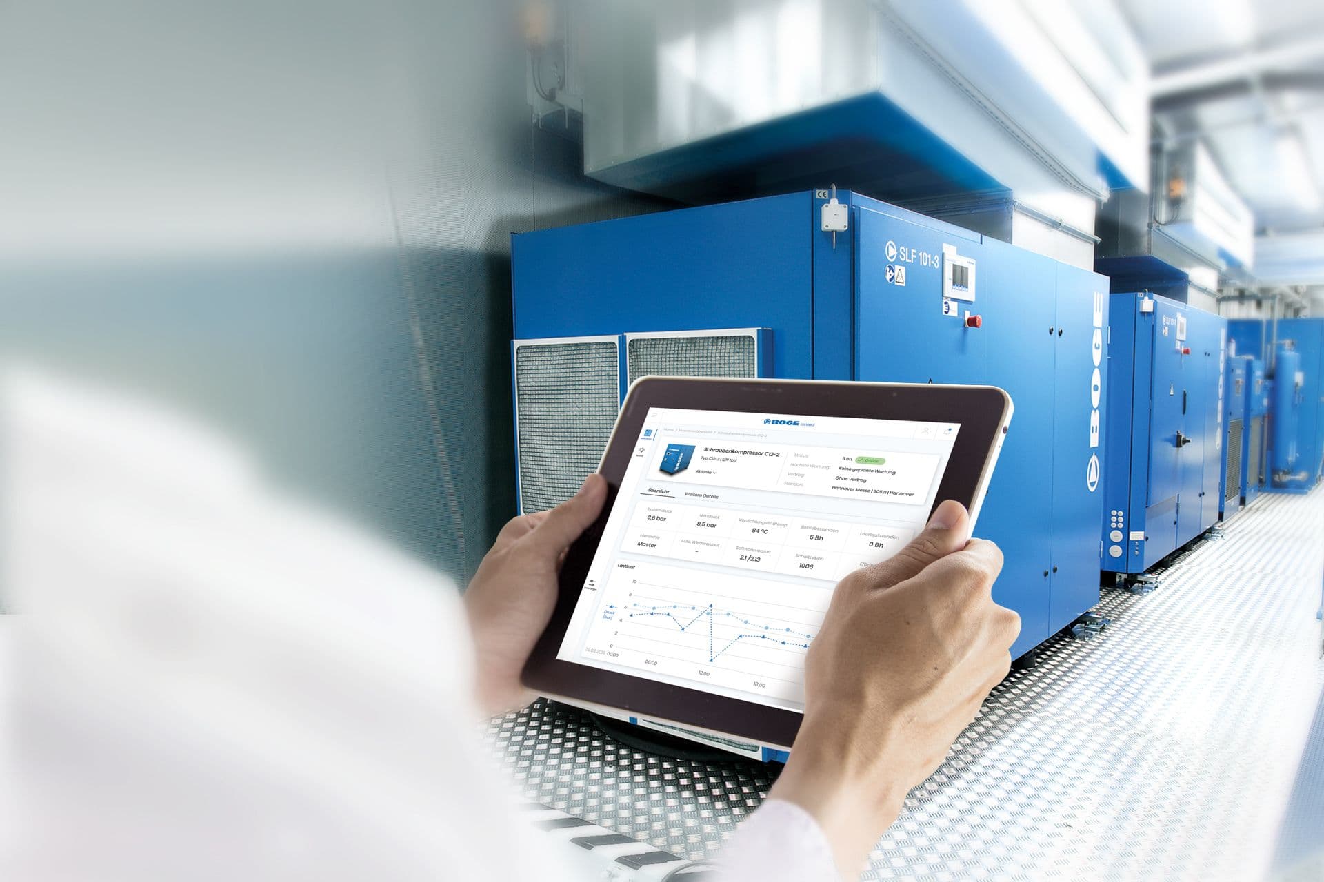 Hände halten ein Tablet mit installiertem Remote Monitoring Tool BOGE onnect von BOGE, im Hintergrund stehen diverse Druckluftanlagen in einer Halle