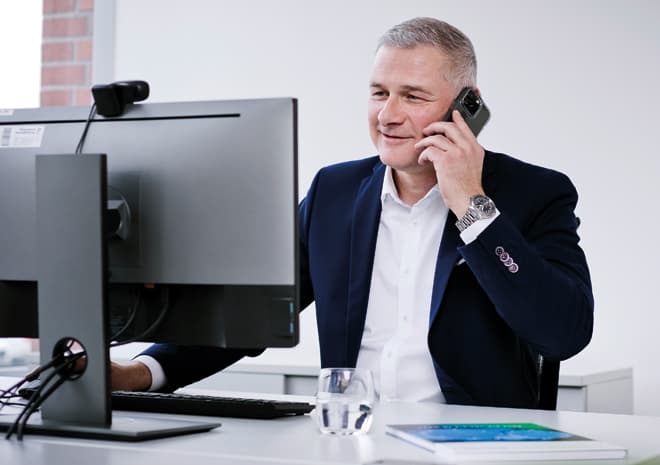 BOGE Finanzierung Ansprechpartner sitzt am Schreibtisch vor einem Computer und führt mit einem Handy ein Beratungsgespräch