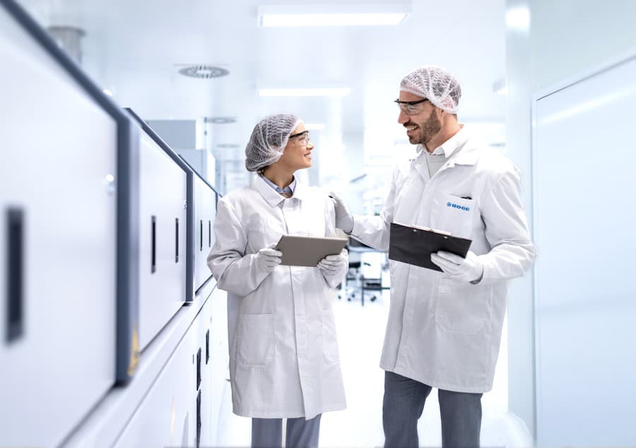 Zwei Moge Mitarbeiter die in einem Gespraech vertieft sind und Kittel und Haube an haben